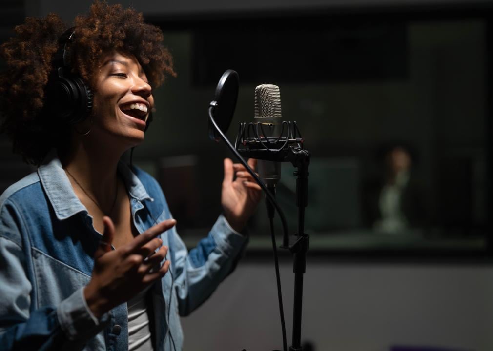 Young female singer wearing headphones recording in a music studio.