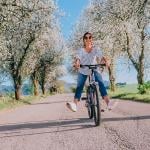 Happy smiling woman riding a bicycle under apple blossom trees.