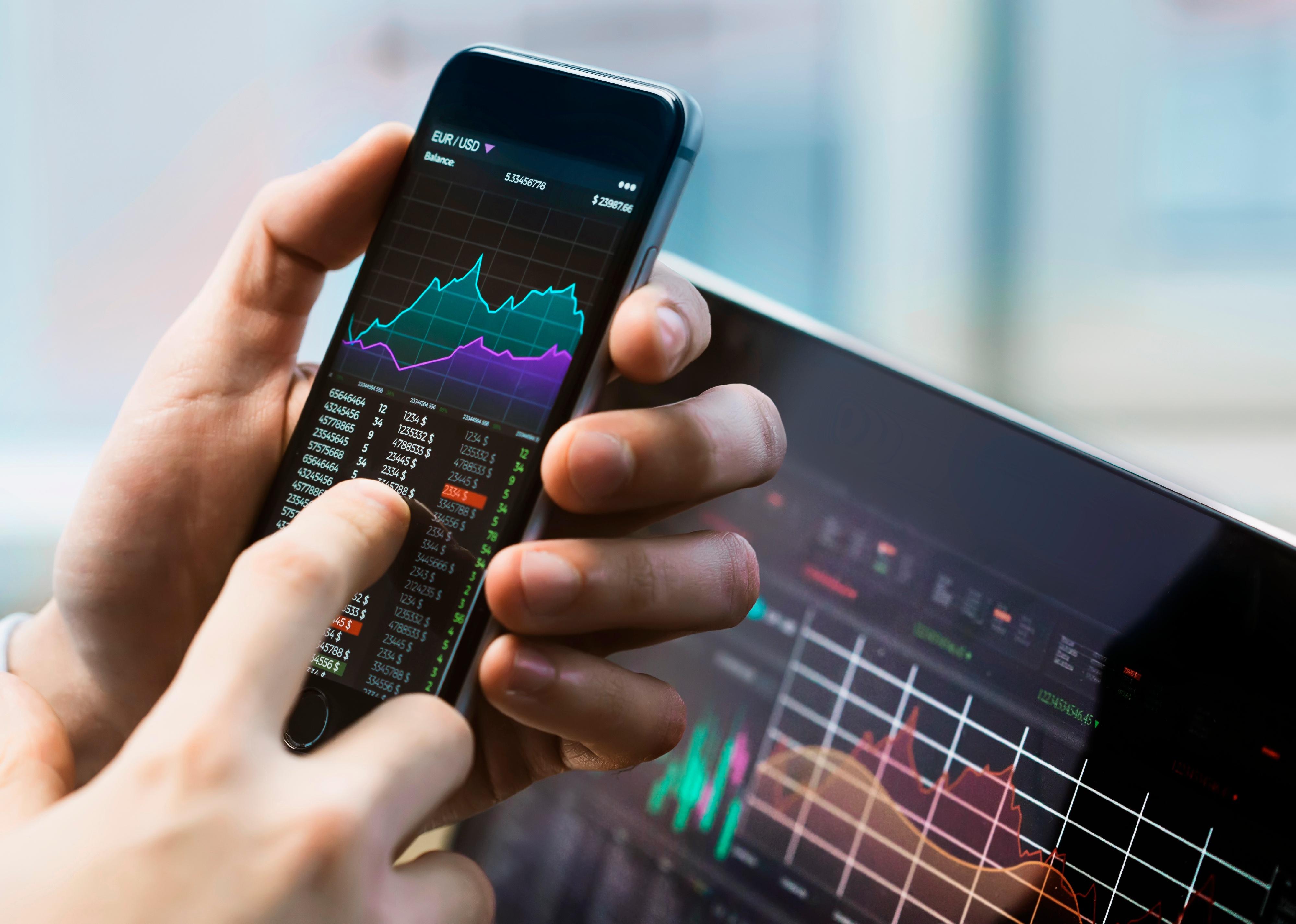 Business man holding phone with stock market displayed.